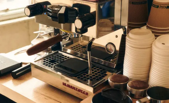 Espresso machine on a counter with stacked coffee cups and tamper tools.