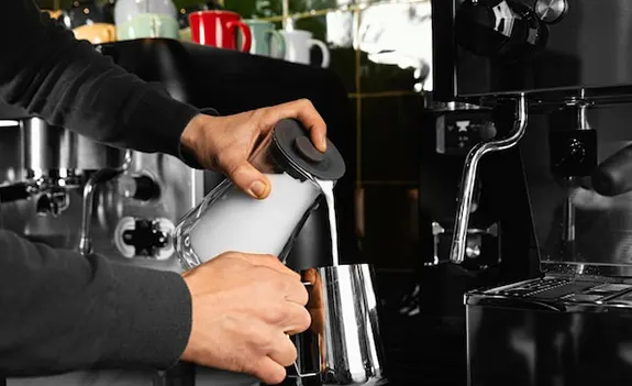 Barista steaming milk with a stainless steel frothing pitcher.