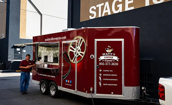 Red mobile coffee truck with open service window and a person standing nearby.