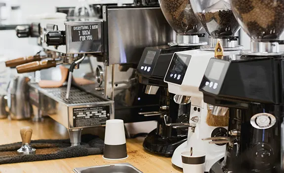 Commercial espresso machines on a countertop with coffee grinders and cup.